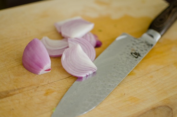 Red onion is thinly sliced on a cutting board.