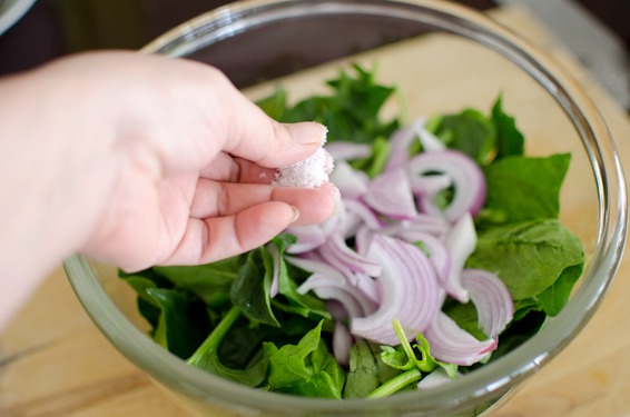 A pinch of salt is added to the spinach and red onion mixture in a bowl.