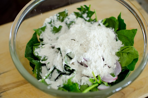 Flour is added to the spinach and red onion mixture in a bowl.