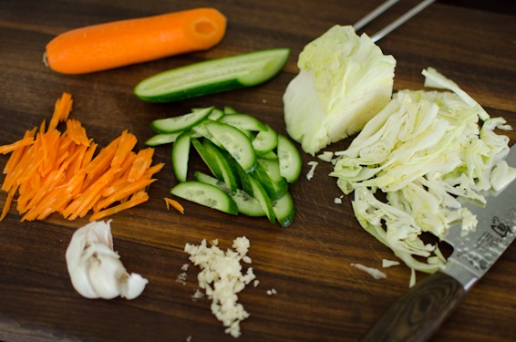Thinly slice cabbage, cucumber, and carrot to make a Korean salad.