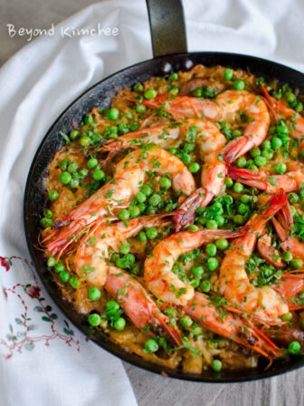 This Korean fusion paella with kimchi, shrimp and peas are cooked in a skillet.