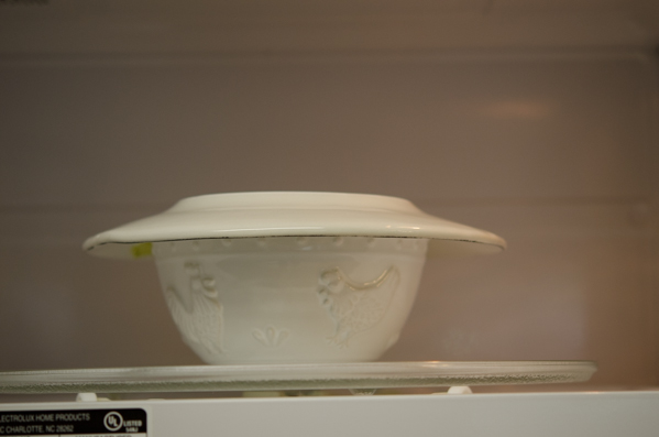 A white bowl of tofu egg mixture is covered with a small plate on top and placed in a microwave.