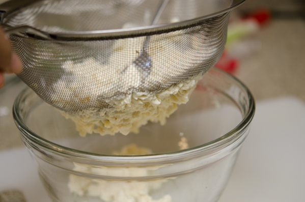A fine mesh strainer is passing through smashed silken tofu.