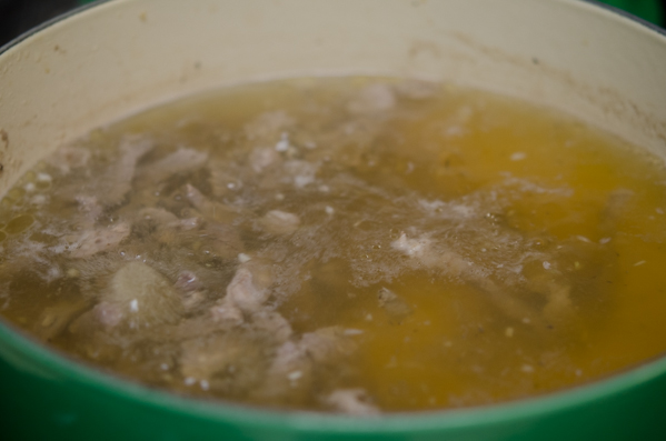 Beef pieces are simmering in a clear broth in a pot.