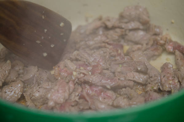 Beef slices are being fried in a pot.