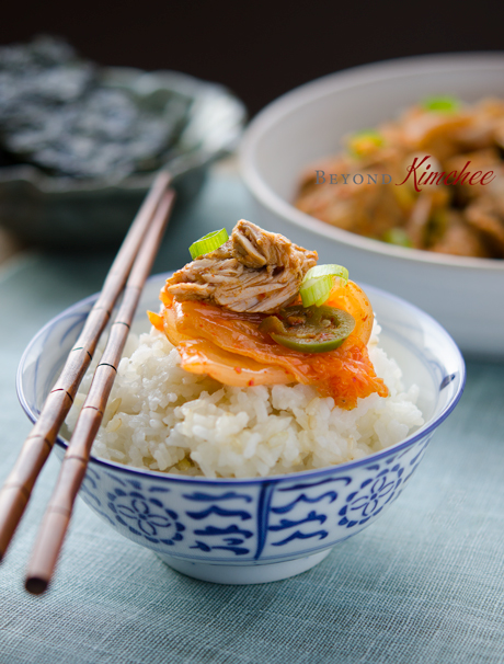 A piece of braised pork ribs and kimchi slices are served on top of rice and chopsticks.