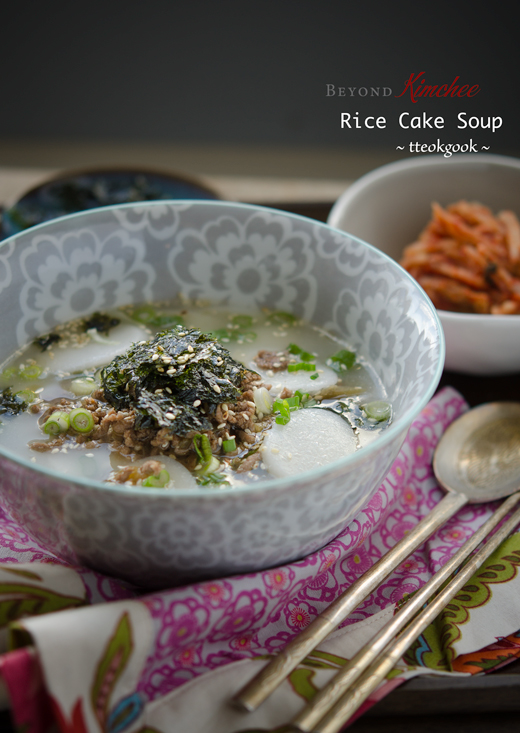 Korean rice cake soup is served with ground beef topping and crumbled seaweed.