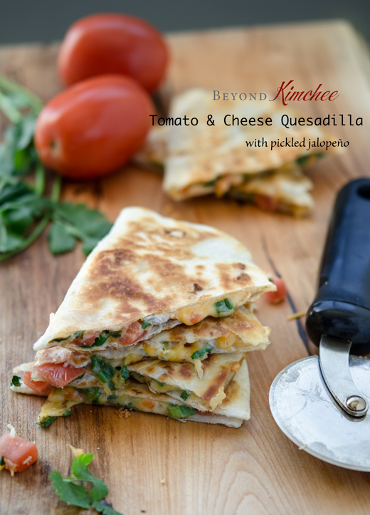 Quesadilla with tomato, cheese, pickled jalapeno is sliced with a pizza cutter.