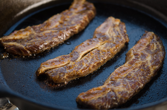 Three beef short ribs are placed on a hot skillet.