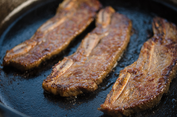 Three beef short ribs are cooked and browned on the surface.