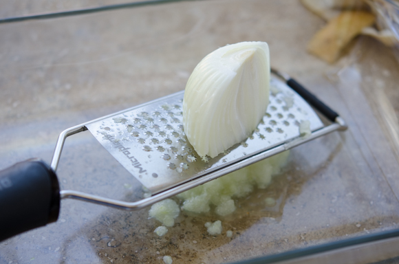 An onion is being grated on a microplane grater.