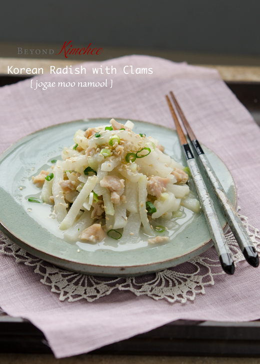 A side dish made with Korean radish and canned clam is served with chopsticks on a pink table mat.