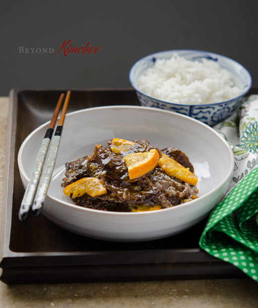 Orange beef is served in a bowl on a tray with rice.