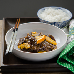 Orange beef is served in a bowl on a tray with rice.