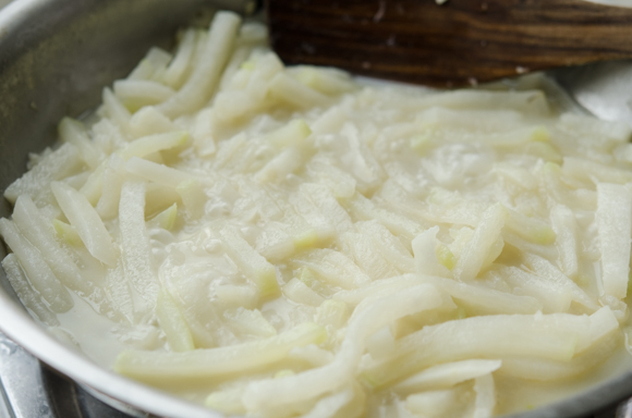 Korean radish is softened in a simmering clam juice in a skillet.