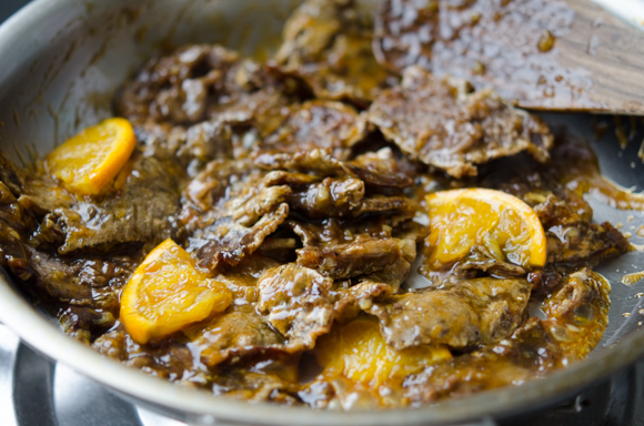 Orange slices are added to a glazed beef in a skillet.