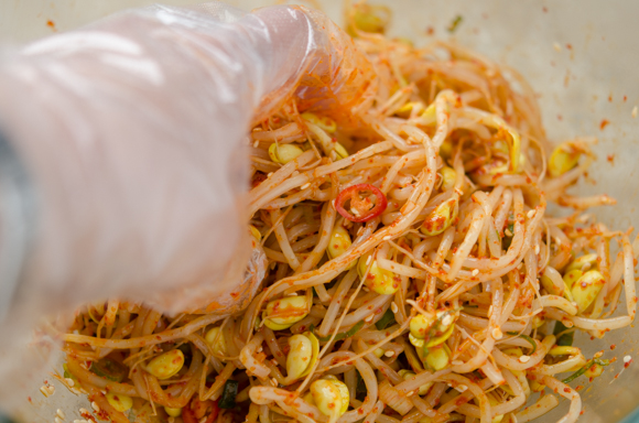 A hand is tossing soybean sprouts with the spicy seasoning.
