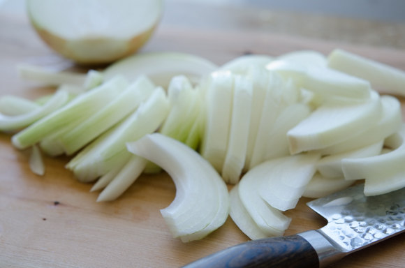Onion is sliced into strips with a knife.