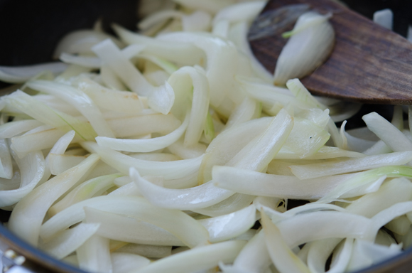 Sliced onion are cooking in a skillet.