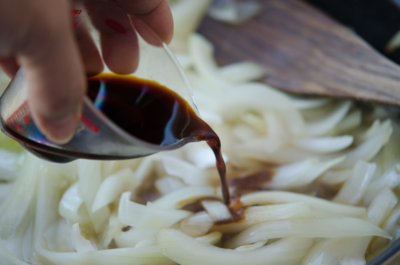Soy sauce is added to cooked onion in a skillet.