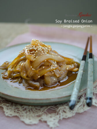 Soy braised onion side dish is served on a green plate with chopsticks.