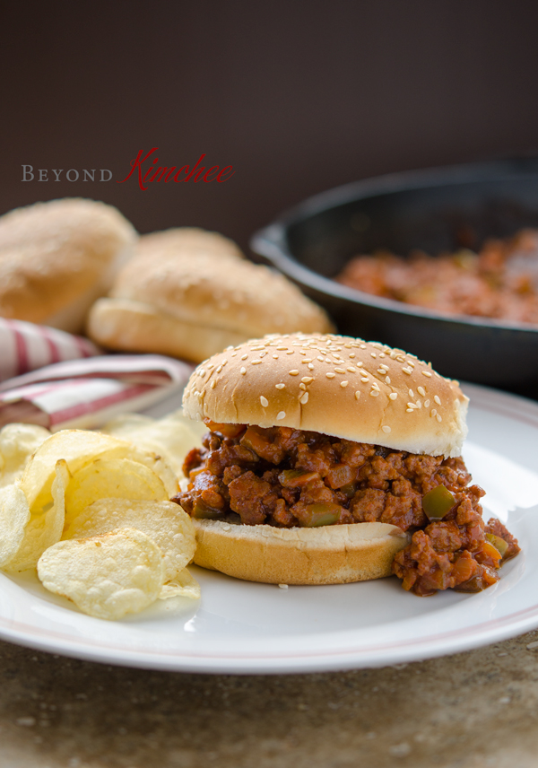This Korean style Gochujang sloppy Joes is served on a bun with potato chips on a plate.