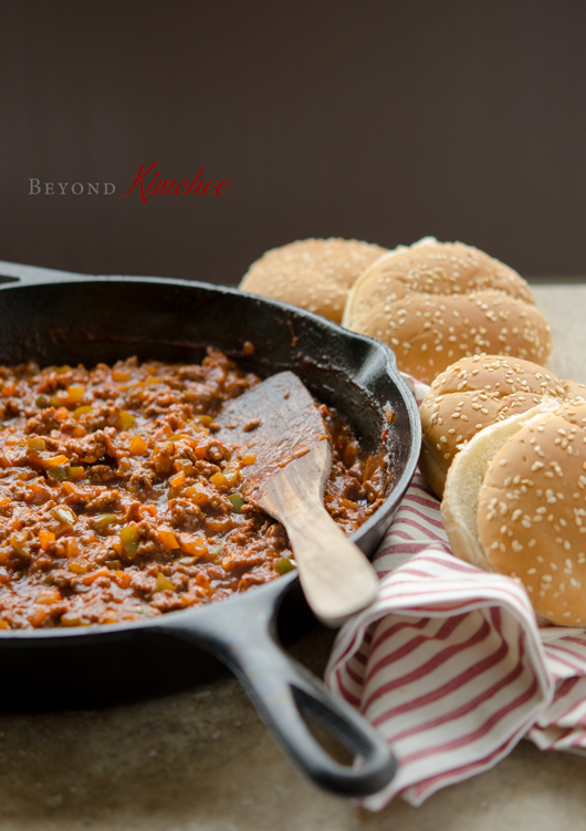 Sloppy Joes sauce made in a cast iron skillet is sitting next to hamburger buns.