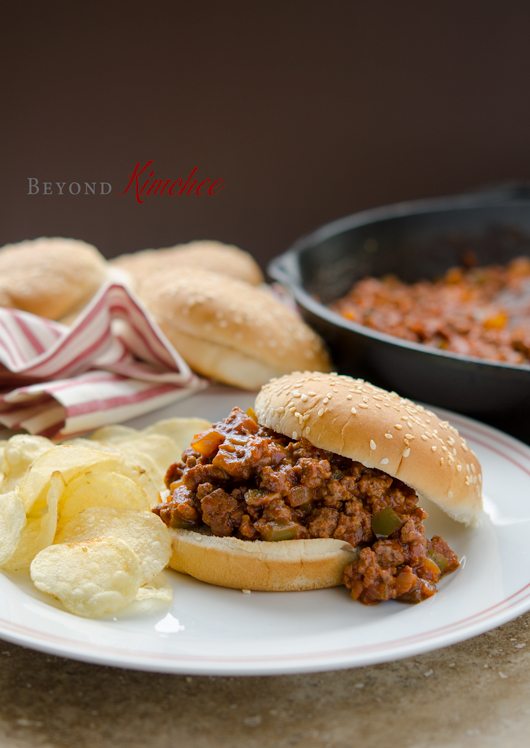 Korean sloppy Joes are spooned in between buns and served with potato chips on a plate.