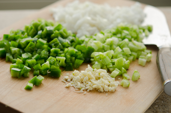 Green pepper, celery, onion, and garlic is finely chopped on a cutting board.