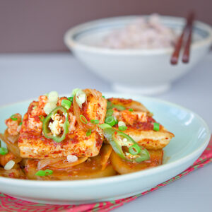 Spicy tofu and radish side dish is garnished with green chili and served with rice.