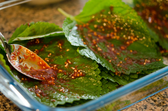 Applying the seasoning sauce to perilla leaves with a spoon.