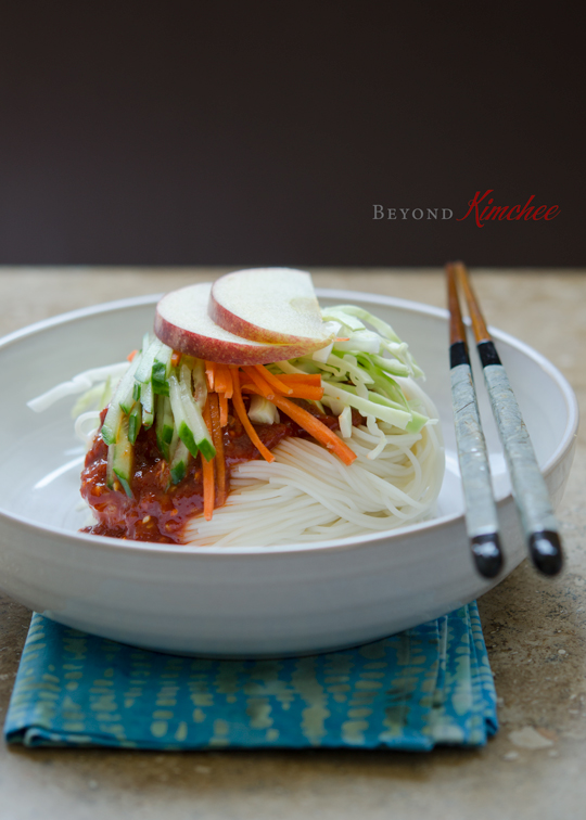 Korean noodles are topped with homemade gochujang sauce, cucumber and carrot slices in a bowl.