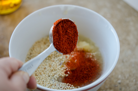 A spoonful of Korean chili flakes is added to the sauce mixture in a bowl.
