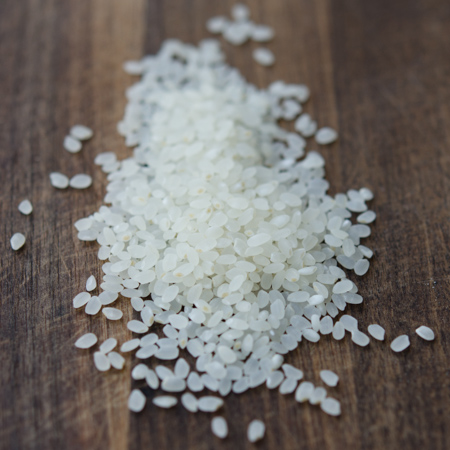 Some short grain white rice is scattered on the wooden board.