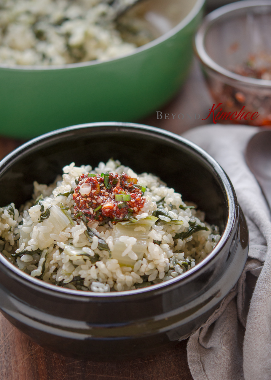 Swiss chard with brown rice topped with chili sauce in a stone pot.