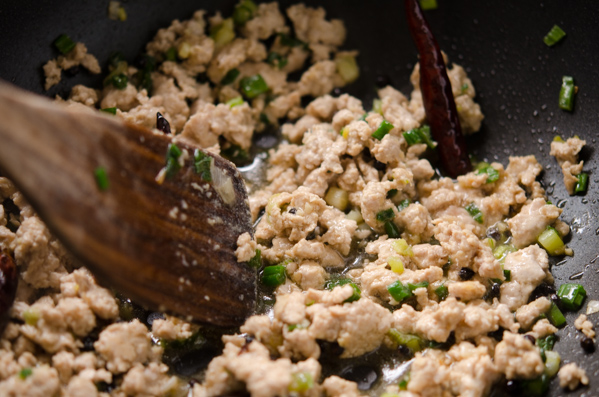 Ground pork is stir-frying in the chili oil and green onion mixture.