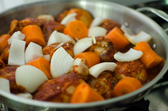 Carrot and onion pieces are added to the Korean chicken stew in a pan.