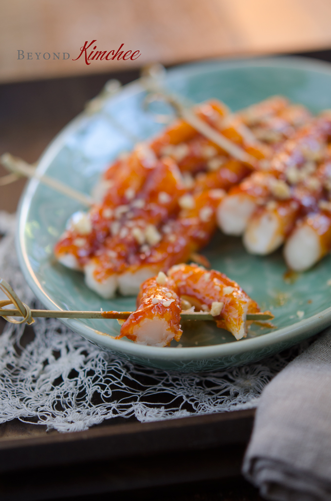 Chewy rice cakes skewers glazed with gochujang sauce are served on a green plate.