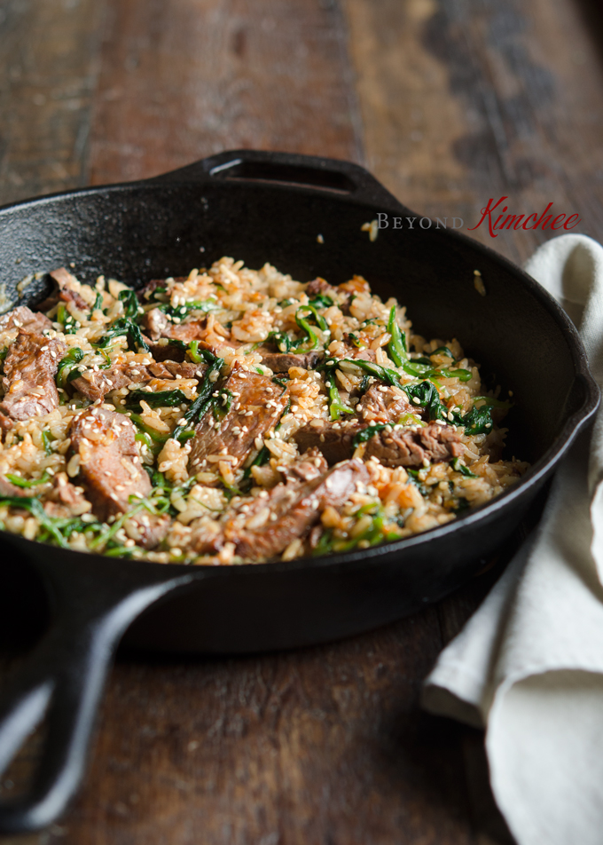 Steak and Spinach Bibimbap is garnished with toasted sesame seeds in a skillet.