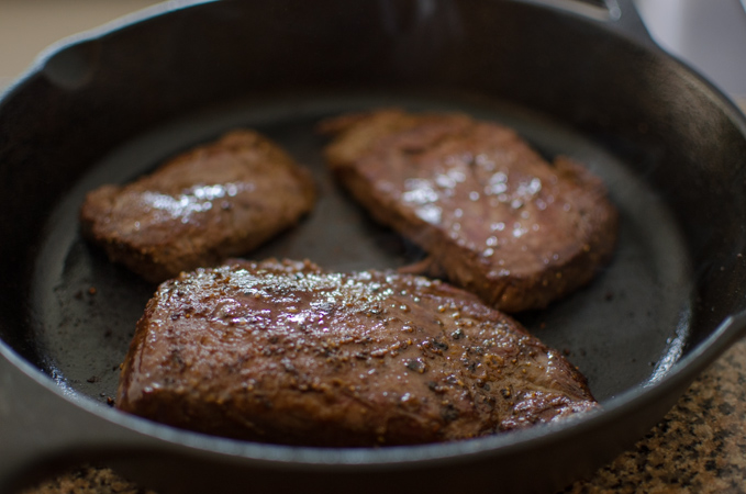 Beef steak is seasoned with salt and pepper and seared in a cast iron skillet.
