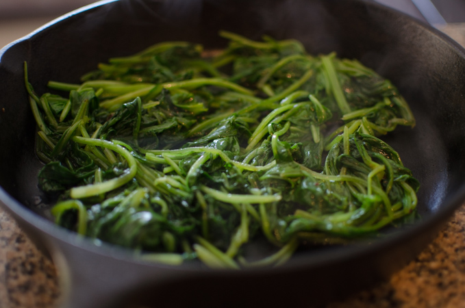 Blanched spinach is placed on a cast iron skillet.