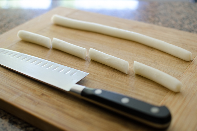 A long rice cake rope is sliced into small size.