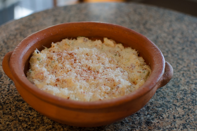 More Parmesan cheese and paprika  is topped over hearts of palm dip mixture in a clay baking dish.