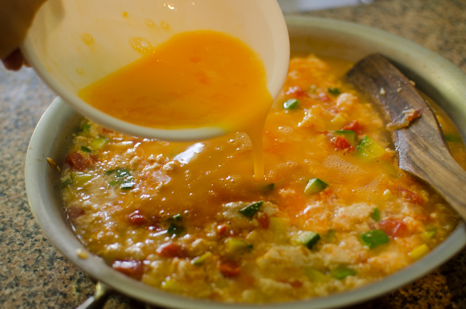 Beaten eggs are added to soft tofu and vegetables in a pan.