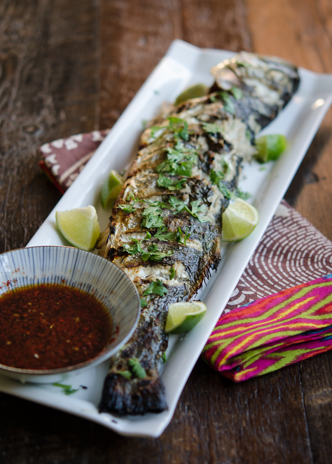 A grilled fish is served on a white plate with soy lime chili sauce