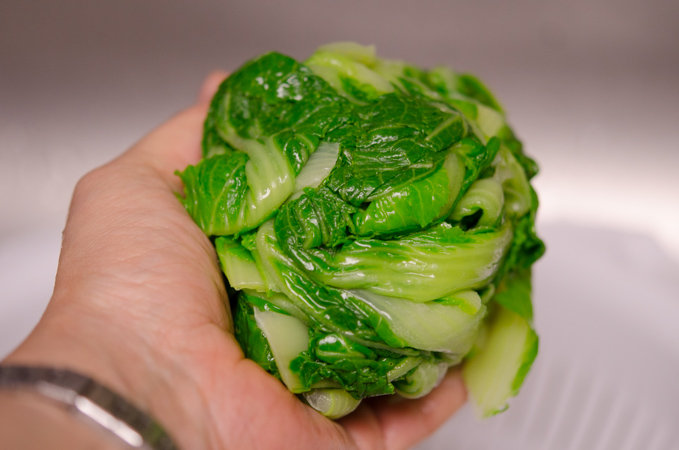 A hand is squeezing out blanched cabbage to remove water