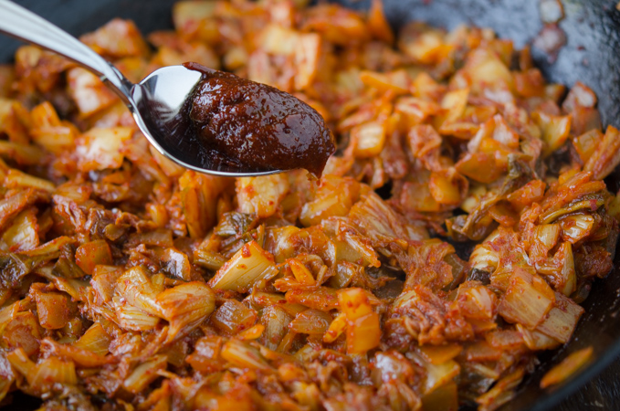 A tiny spoonful of gochujang is added to fried kimchi mixture in a skillet.