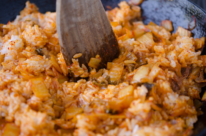 A wooden spatula is breaking down the grain of rice to make kimchi fried rice.