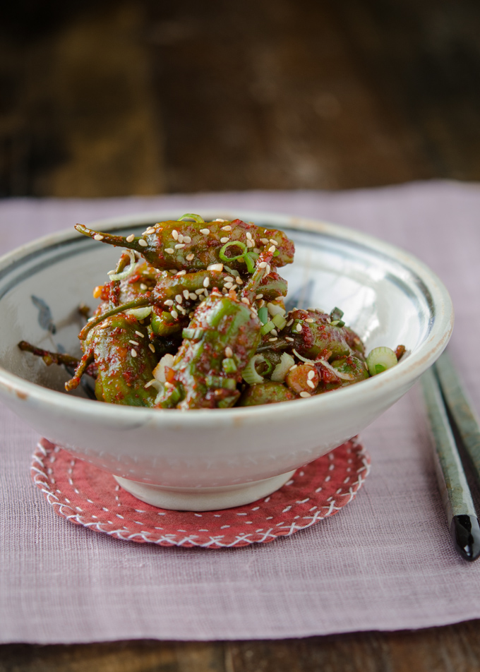 Steamed shishito peppers are served in a bowl and presented over a linen place mat.