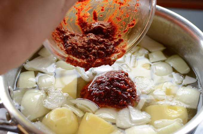 Spicy seasoning is added to potato and onion in a pot.